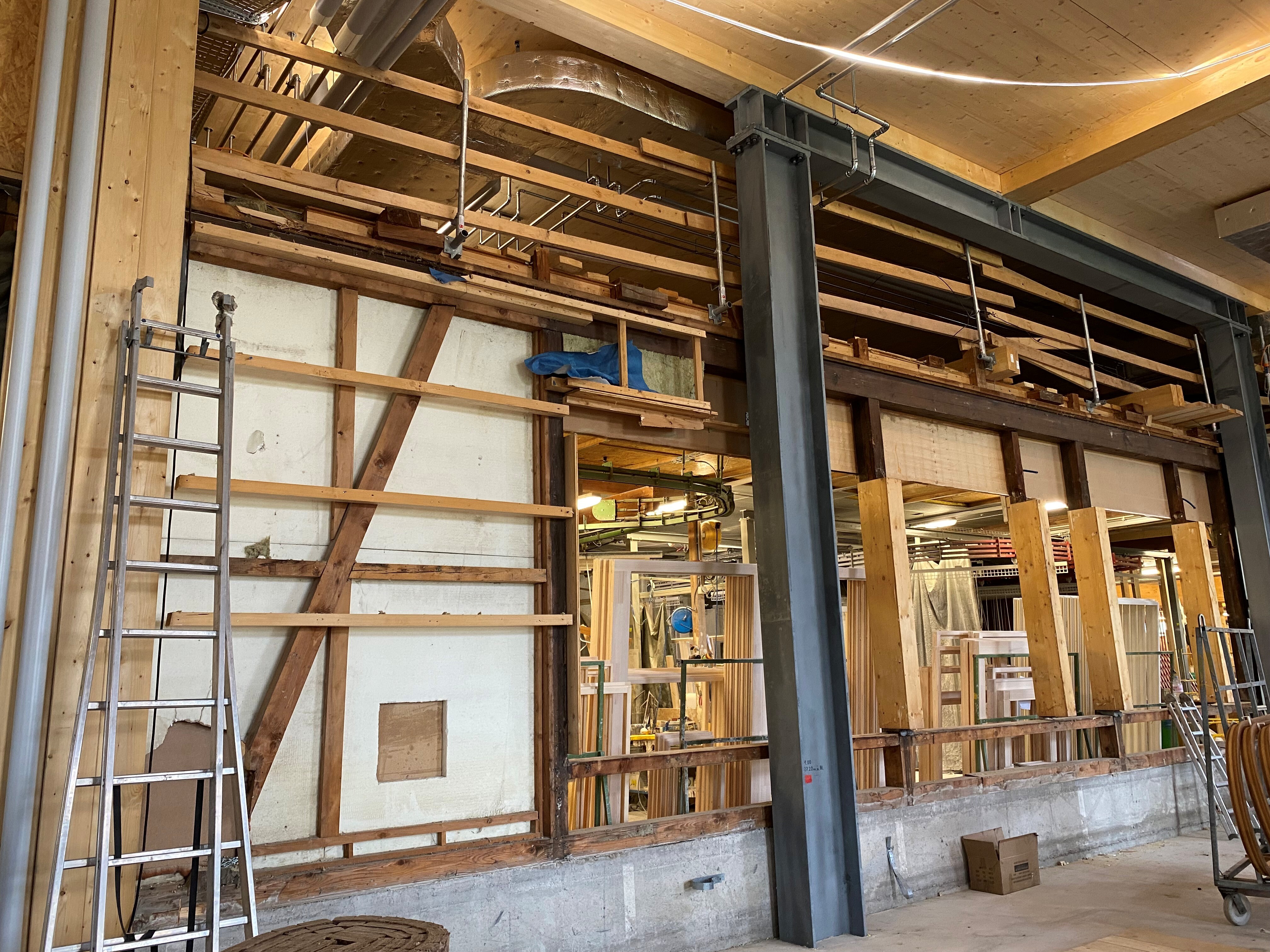 Während draussen die Fassade montiert wird, schreiten auch die Arbeiten im Innern des Rucksacks zügig voran. Die bisherige Gebäudehülle des bestehenden Gebäudes wird Schritt für Schritt zurückgebaut und macht Platz für die neue Verbindung zwischen Bestand und Erweiterungsbau. Dadurch wachsen die beiden Gebäudeteile immer stärker zusammen. Mit dem bereits fertiggestellten Hallenboden im Erdgeschoss werden die zukünftigen Produktionsflächen zunehmend erkennbar und die neuen Raumstrukturen nehmen weiter Form an.
